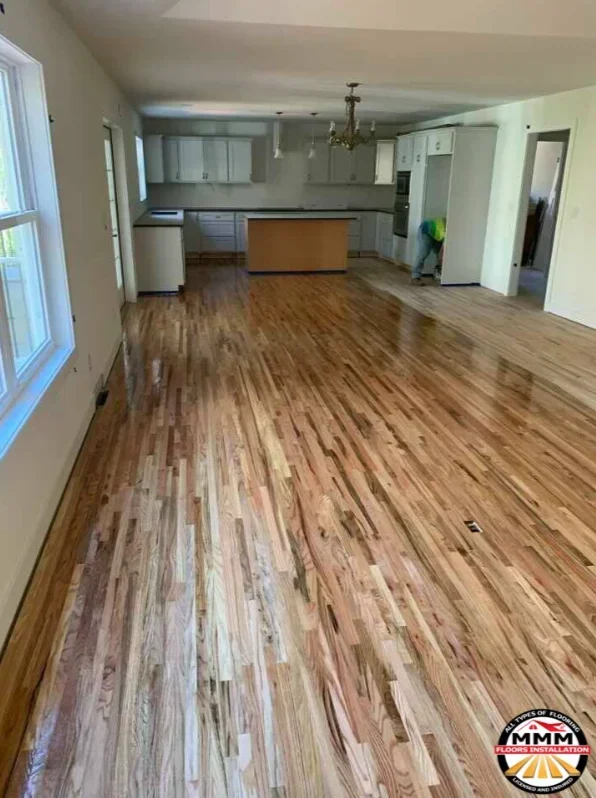 Newly installed hardwood flooring in warm wood tones throughout open living and kitchen area