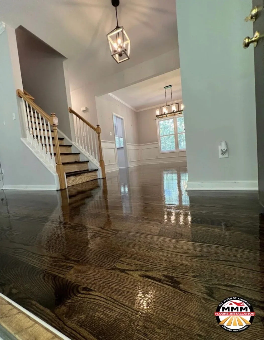Dark engineered hardwood flooring in two-story foyer with oak staircase and white wainscoting