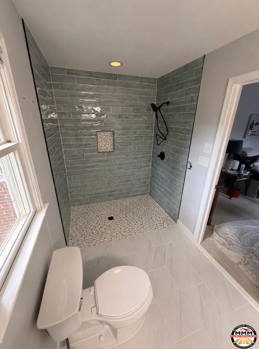 Walk-in shower with gray subway tile walls, pebble stone floor, and white ceramic tile bathroom flooring
