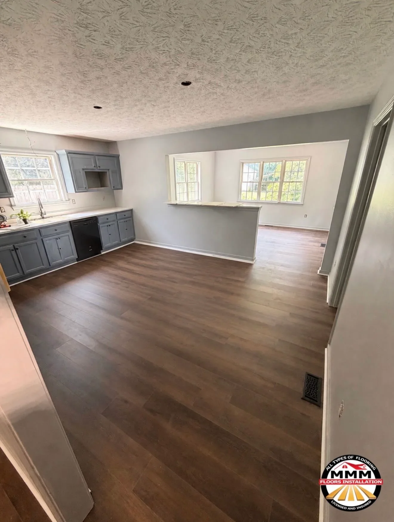 Dark hardwood flooring installed in kitchen and living room with gray cabinets and white walls