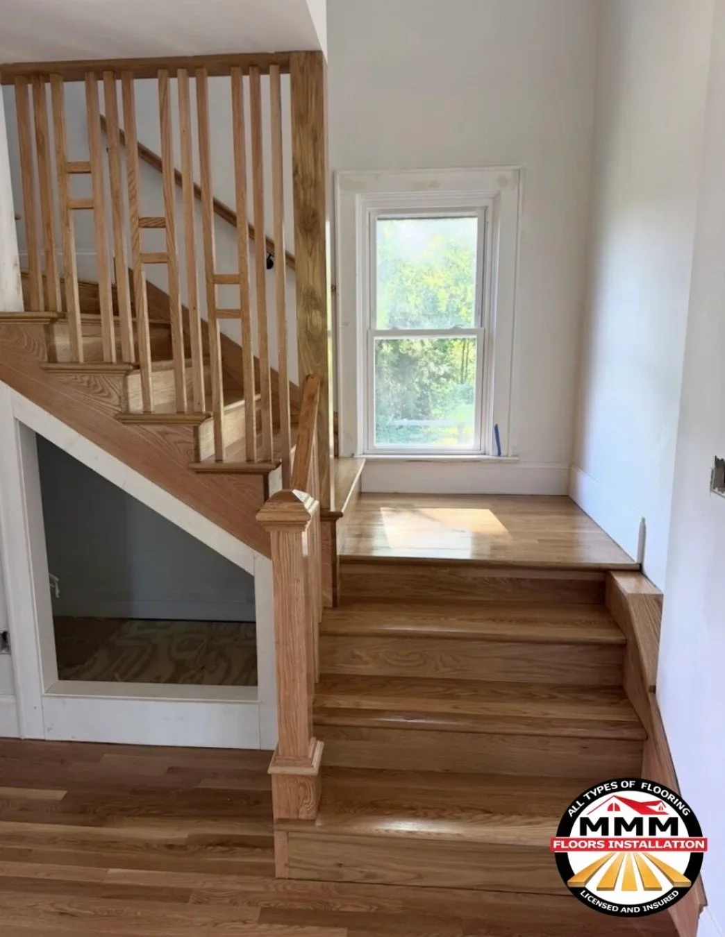 Oak hardwood flooring with custom wooden staircase, vertical spindles, and newel posts in bright entryway