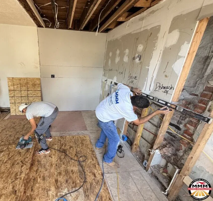 Two workers installing OSB subfloor and preparing basement space for flooring with drywall framing
