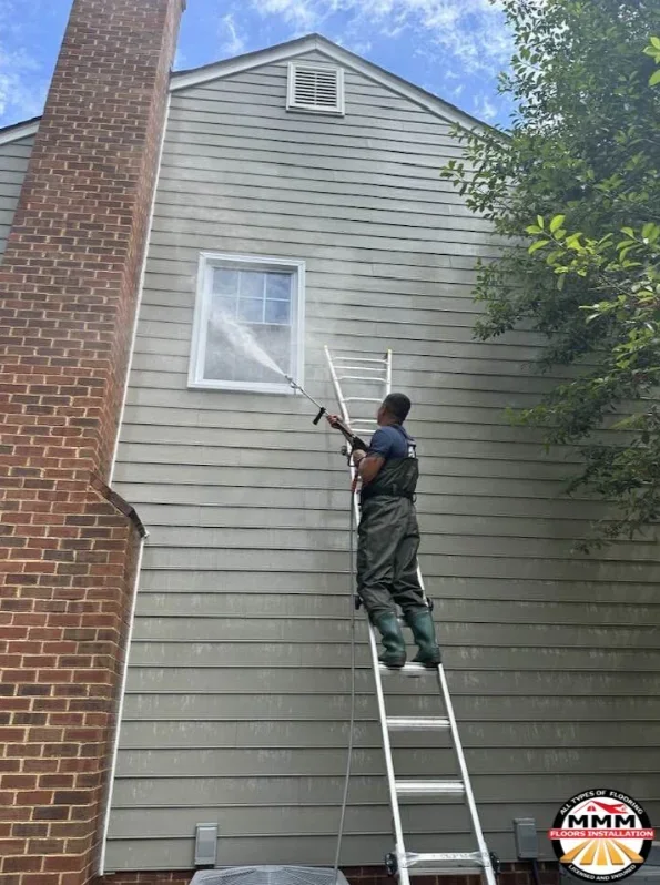 Worker on ladder cleaning gray vinyl siding and white soffit vent on residential home exterior
