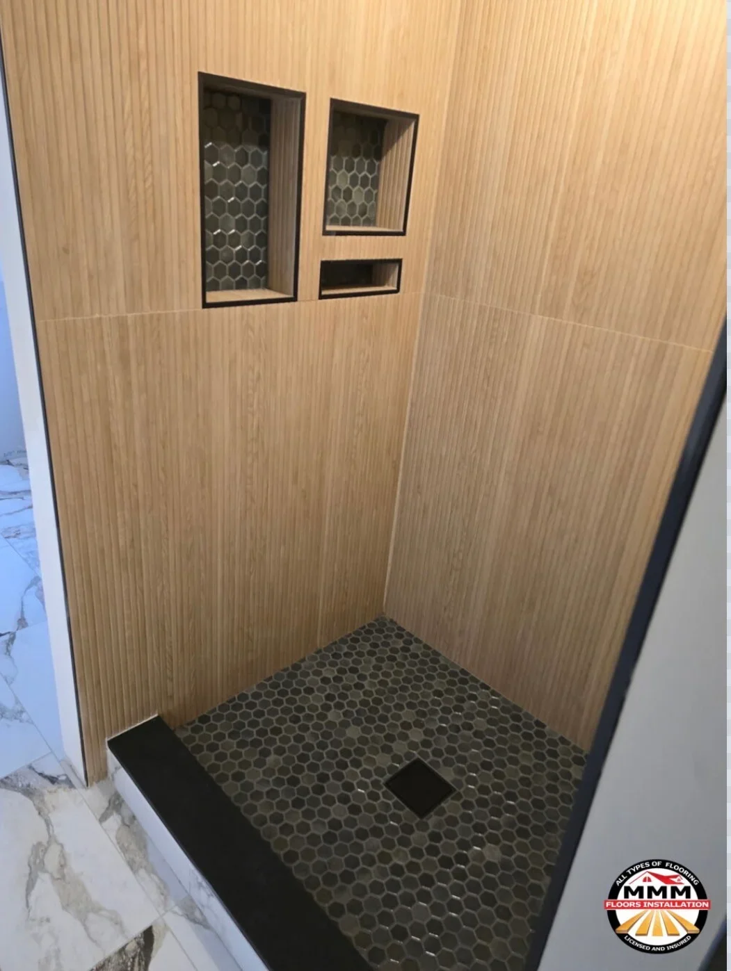 Gray hexagonal tile shower floor with black trim and wood-grain wall panels