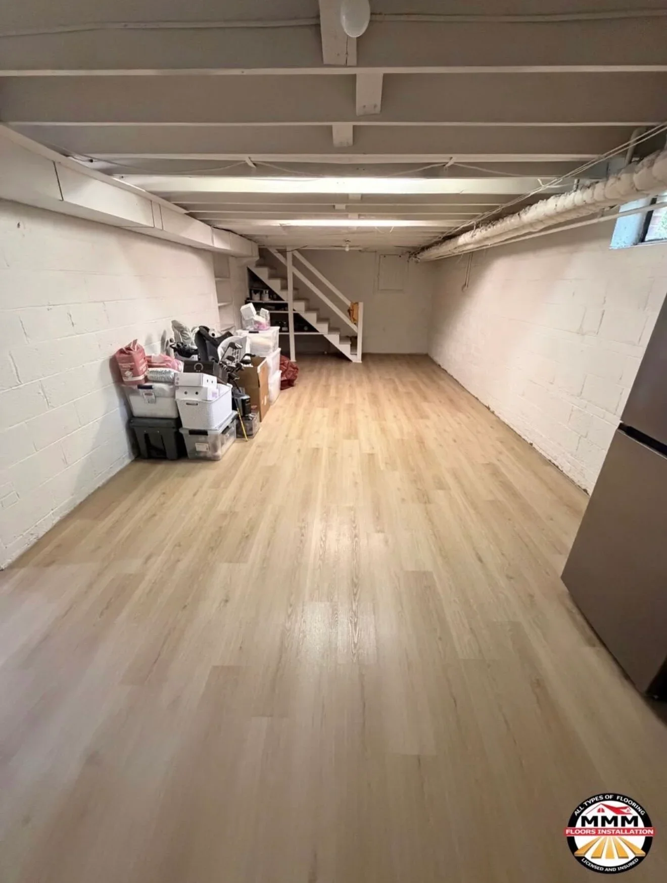 Luxury vinyl plank flooring installed in basement with white block walls and exposed ceiling beams