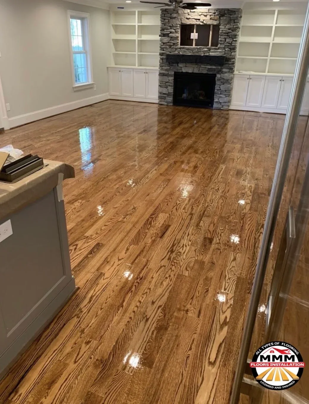 Polished hardwood floor installation in living room with stone fireplace and white cabinetry