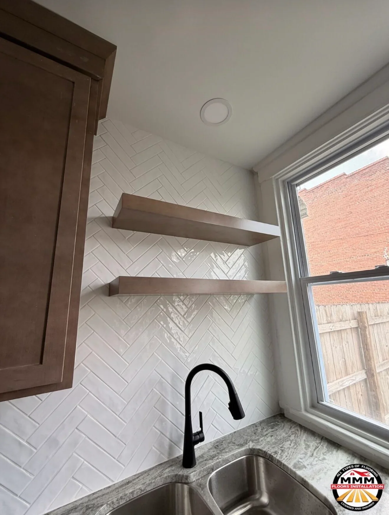 White herringbone subway tile backsplash with floating shelves and black faucet